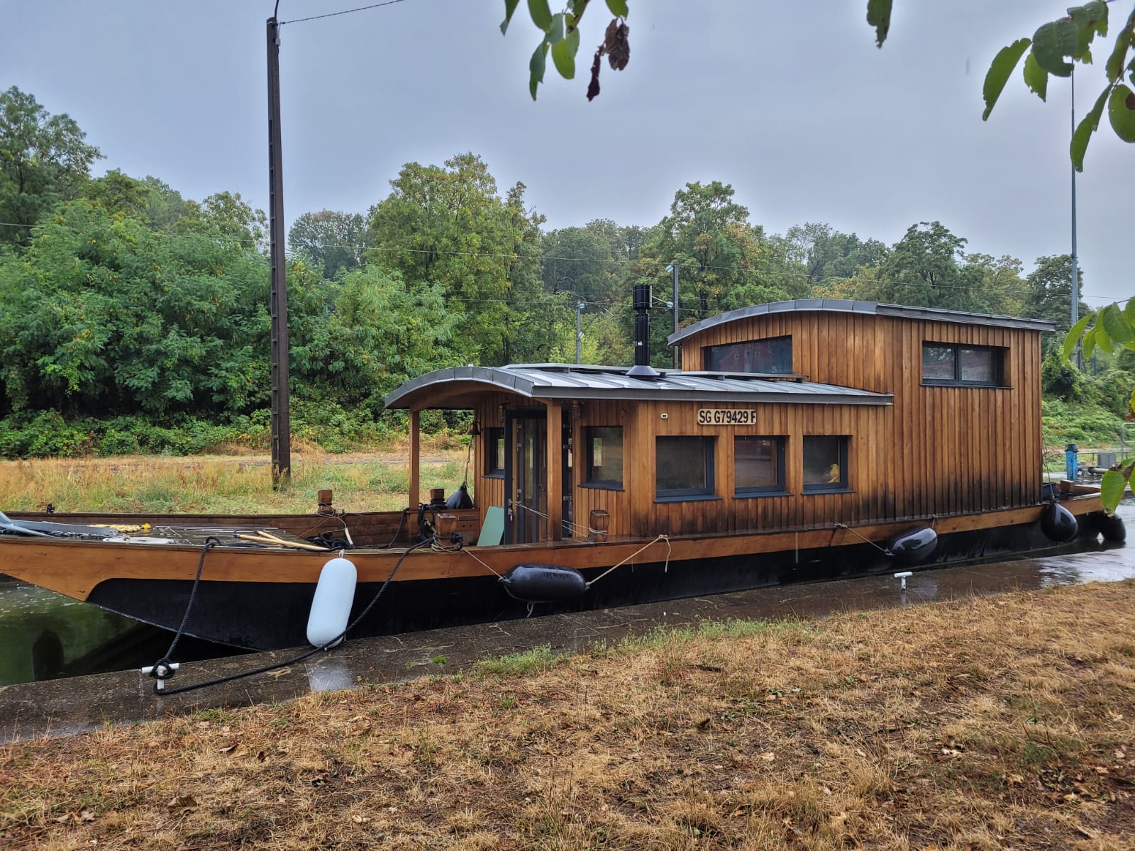 Le bateau amarré le long du canal, coque noire et superstructure en bois